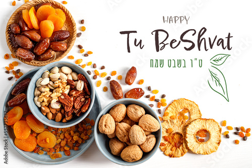 Mix of dry fruits and nuts   in a wicker plate, branch with young green leaves. Concept of the Jewish holiday. Vertical banner with the inscription Tu Bishvat in English and Hebrew