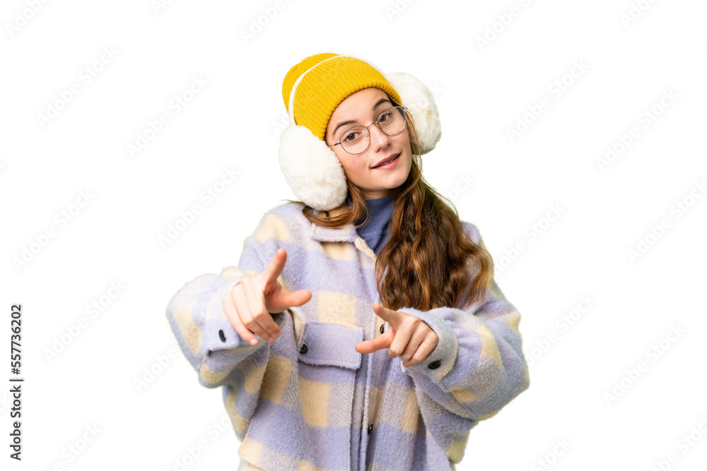 Teenager girl wearing winter muffs over isolated chroma key background points finger at you while smiling Teenager girl wearing winter muffs over isolated chroma key background points finger at you while smiling