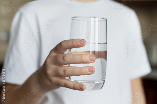 The girl holds a glass of clean water in her hand. The hand reaches forward. The concept of drinking clean water
