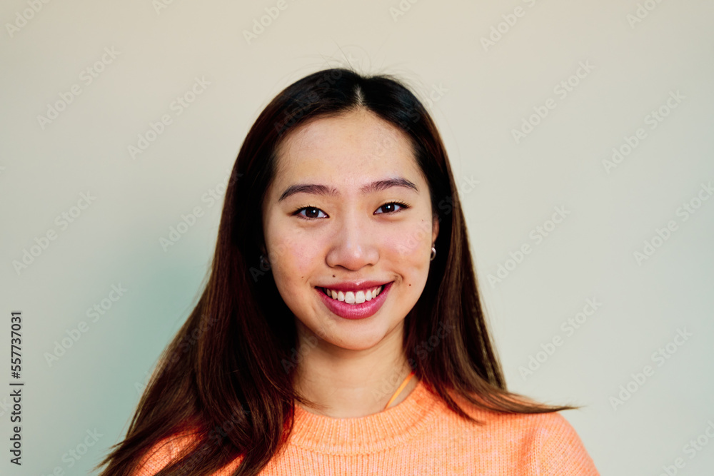 Cheerful Asian female in pink sweater smiling and looking at camera while standing on cream background in studio Cheerful Asian female in pink sweater smiling and looking at camera while standing on cream background in studio
