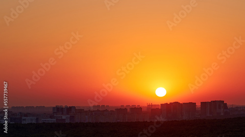 A big red sun in the sunset sky over the roofs of buildings  urban landscape. Evening sky in bright sunlight over the twilight city