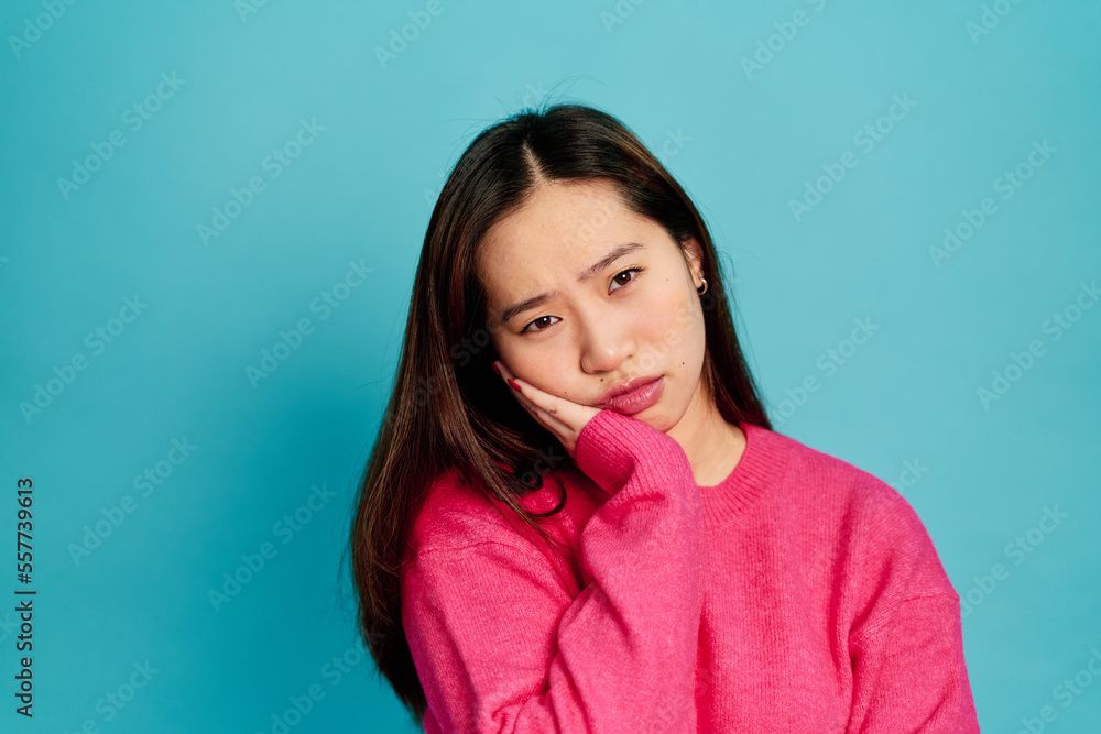 Positive young female in pink sweater looking at camera with astonished face expression while standing on blue background in studio Positive young female in pink sweater looking at camera with astonished face expression while standing on blue background in studio