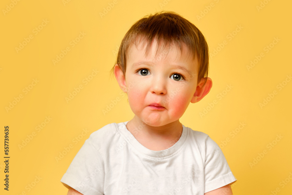 Portrait of an upset toddler baby with a surprised sad face on a studio yellow background. Offended child with disheveled hair in a white t-shirt. Kid aged one year and four months Portrait of an upset toddler baby with a surprised sad face on a studio yellow background. Offended child with disheveled hair in a white t-shirt. Kid aged one year and four months