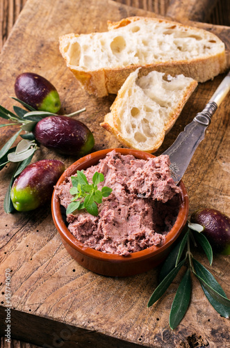Traditional French goose pate as spread in a bowl with baguette and olives served as close-up on a rustic wooden board photo