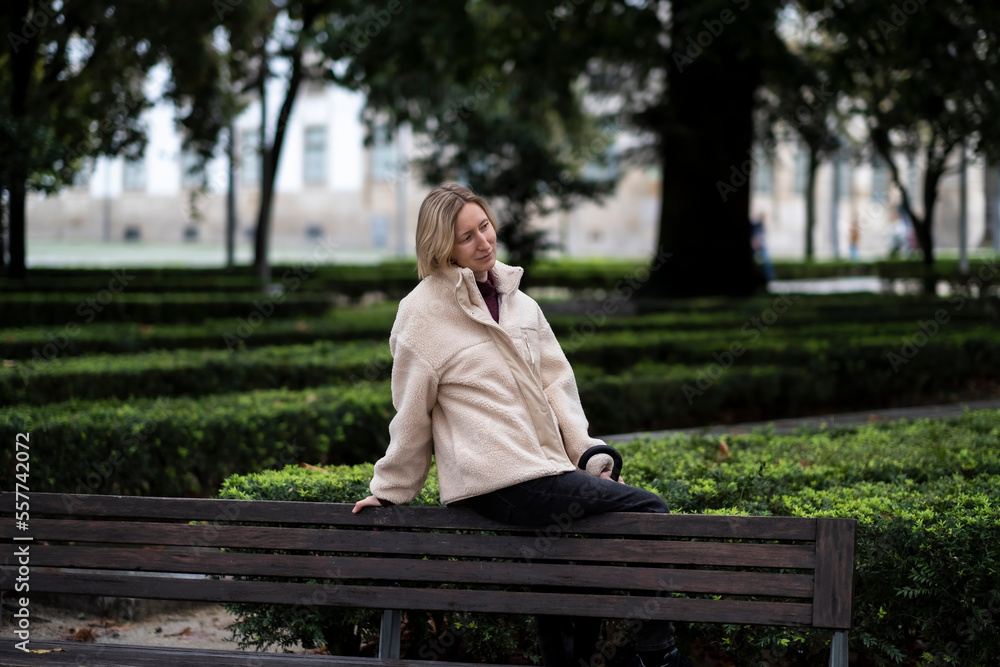 Fototapeta premium A woman sits on the back of a city park bench.