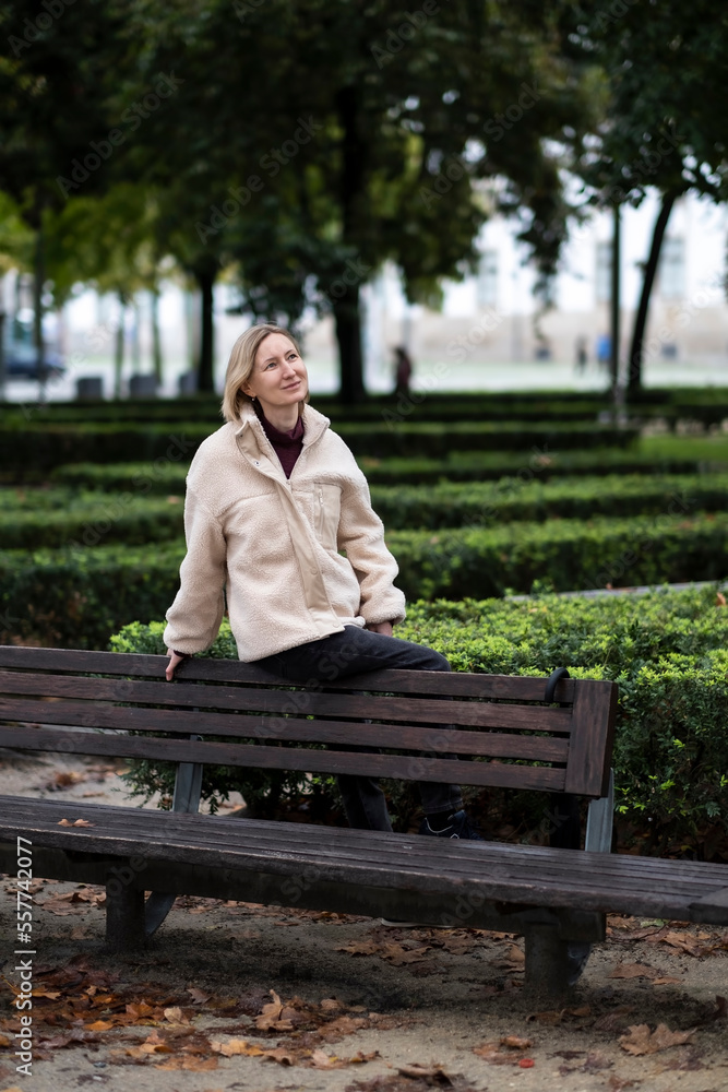 Fototapeta premium A woman sits on the back of a park bench.