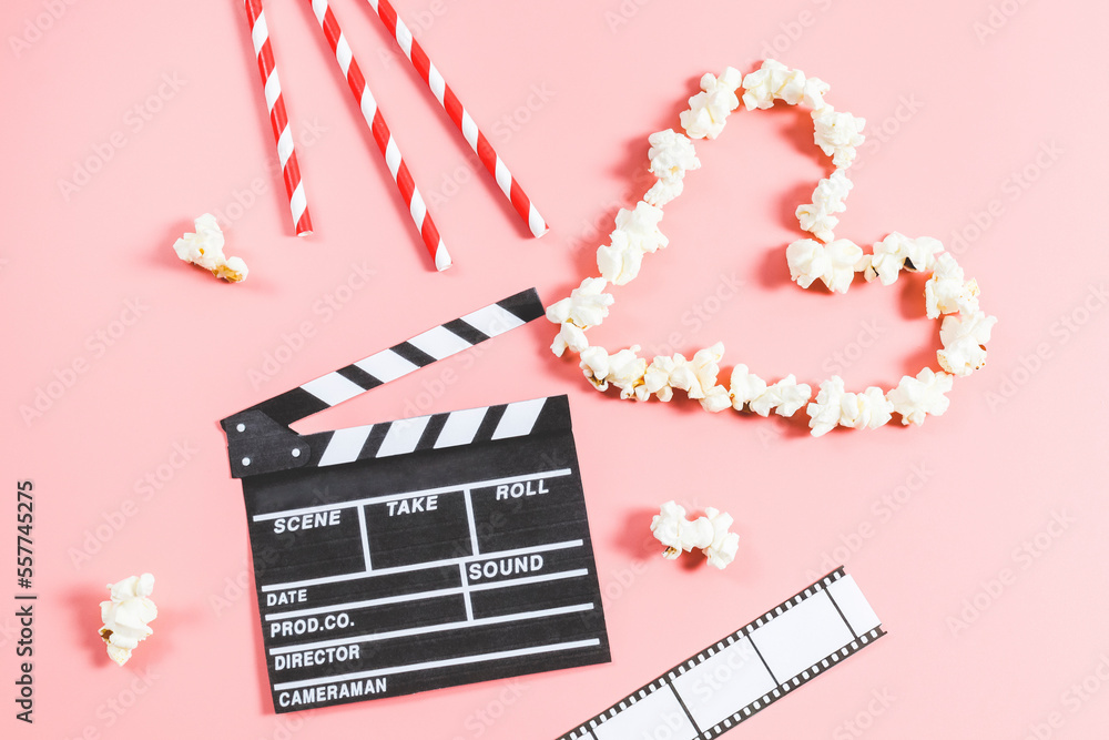 Movie clapperboard, straws, film strip and popcorn in the shape of a heart lies on a pink background