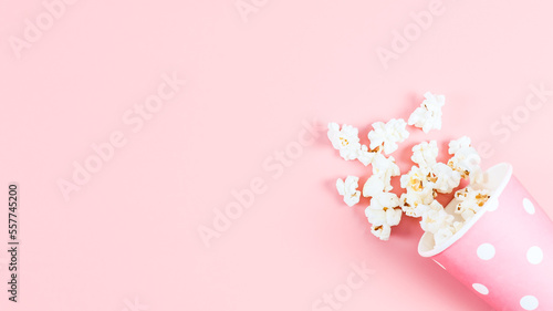 One paper cup with scattered popcorn on a pink background