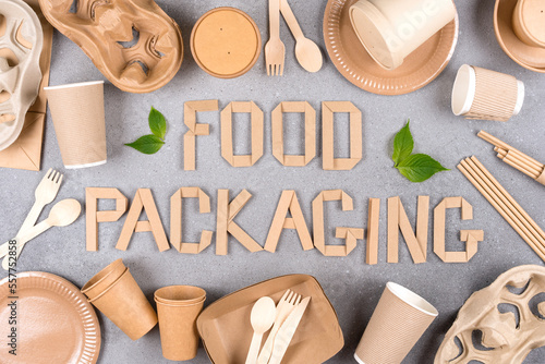 Text FOOD PACKAGING with various paper utensils around over gray concrete background. Eco tableware, sustainable food packaging concept