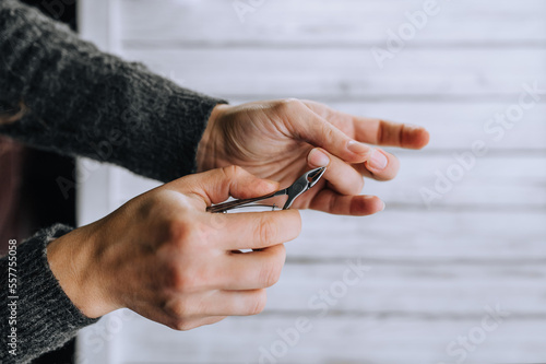 Hands of a woman, a girl close-up, making herself a manicure, cutting cuticles with special scissors on fingers, nails on a wooden white background. Close-up photography, work, beauty, art.