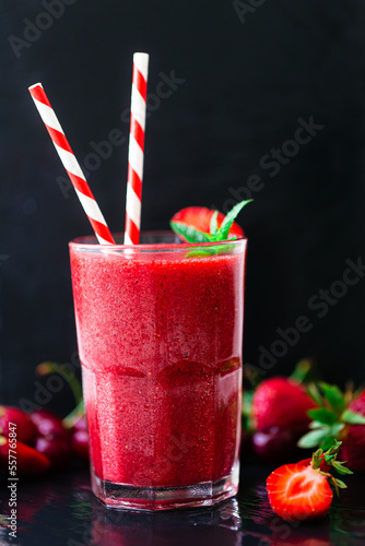 Front view of berry juice or smoothie with fresh strawberries and cherries on dark background.