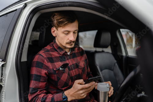 man hold cup with coffee use mobile phone sit in the car take a brake