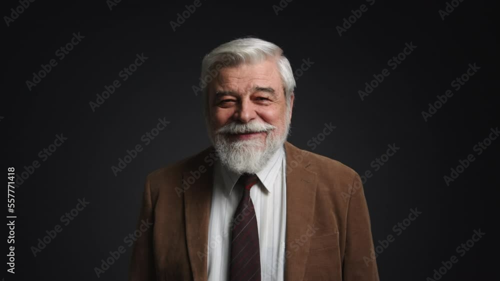 Portrait of gray-haired adult smiling and looking happy. Close-up view of a man in his 60s looking at camera with isolated black background behind. High quality 4k footage Portrait of gray-haired adult smiling and looking happy. Close-up view of a man in his 60s looking at camera with isolated black background behind. High quality 4k footage