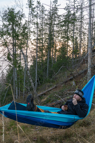 A young man in a hammock drinks coffee and eats cookies.