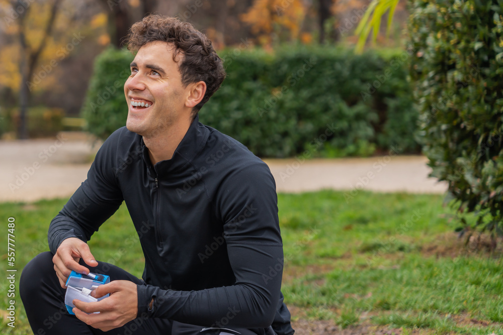 Positive male in casual clothes smiling and looking away while sitting on grass in green park Positive male in casual clothes smiling and looking away while sitting on grass in green park