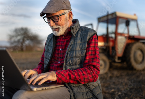 Happy farmer working on laptop in front of tractor
