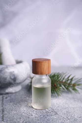 Bottle of aromatic essential oil and mortar with pine branch on light grey table, closeup. Space for text