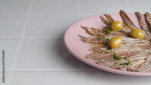 Canned anchovy fillets with olives on white tiled table, space for text