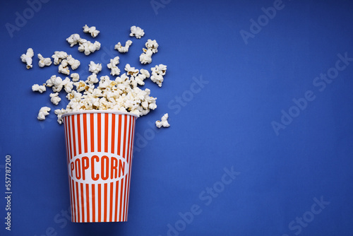 Bucket of tasty popcorn on blue background, flat lay. Space for text