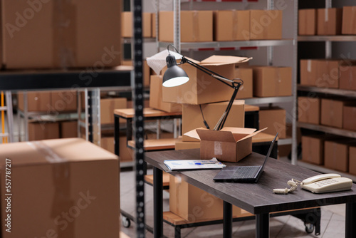 Картината върху платно Empty storehouse with nobody in it equipped with tall shelves full with cardboard boxes ready for delivery, shipping documents standing in desk