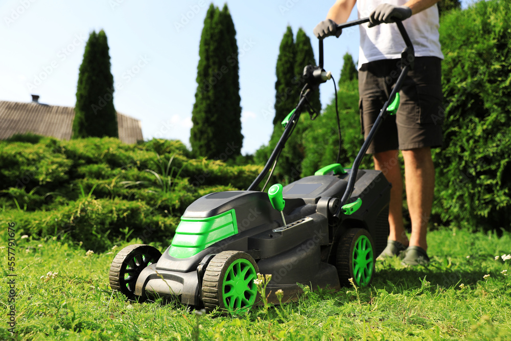 Man cutting grass with lawn mower in garden on sunny day, closeup Man cutting grass with lawn mower in garden on sunny day, closeup