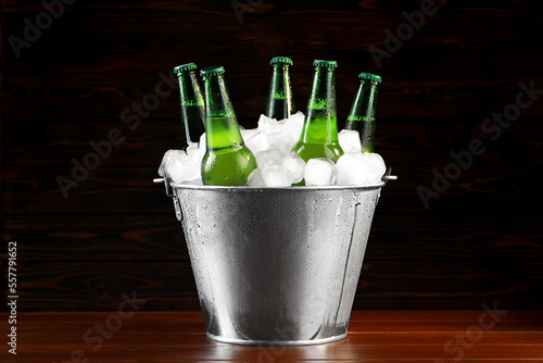 Metal bucket with bottles of beer and ice cubes on wooden background photo