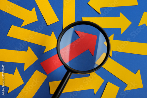 Recruitment process, searching for employee. View through magnifying glass of red paper arrow among yellow ones on blue background, flat lay