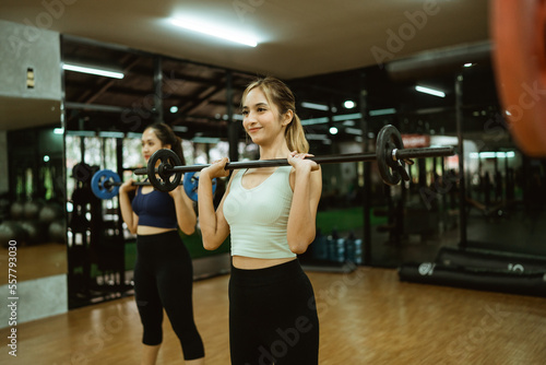attractive young woman lifting barbell in front of chest during exercise in fitness room