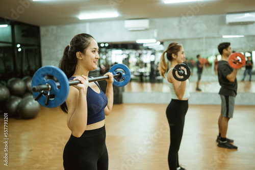 asian woman lifting barbell during group exercise in fitness room