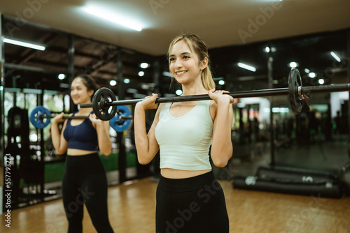 Attractive woman smiling while lifting barbell in front of chest in fitness room