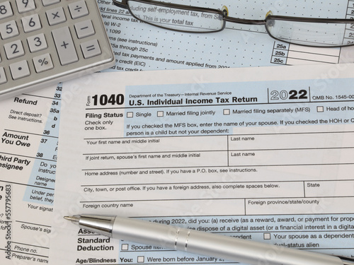 An IRS 1040 tax year 2022 form is shown in 2023, along with an ink pen, calculator, and glasses. The Internal Revenue Service tax filing deadline is April 18 this year.
