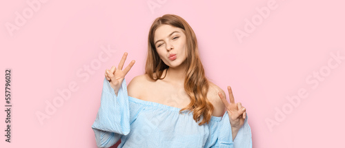 Funny young woman showing victory gesture on pink background