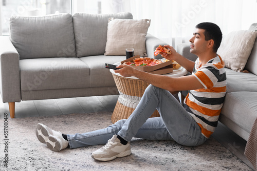 Young man with tasty pizza watching TV at home