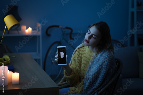 Young woman with discharged mobile phone at home during blackout