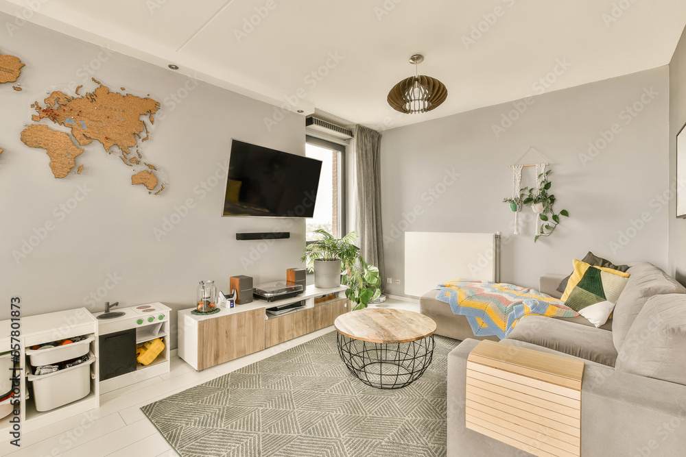 Fototapeta premium a living room with a map on the wall and a grey couch, coffee table, planters, and tv