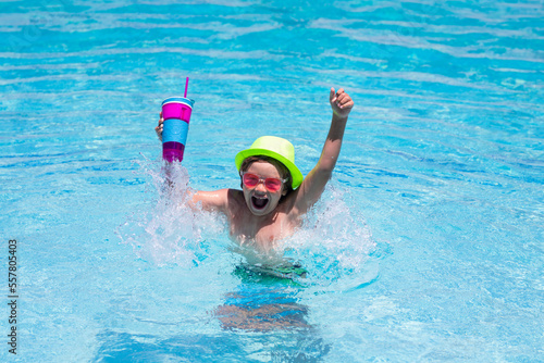 Cute child in hat and sunglasses swim in pool with blue water background. Happy summer holidays. Kid hold cocktail. © Volodymyr