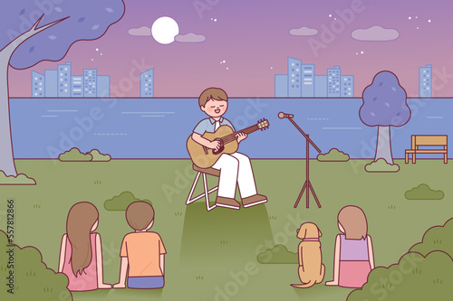 A singer playing an acoustic guitar is busking in the park. People are sitting on the grass and listening to music. photo