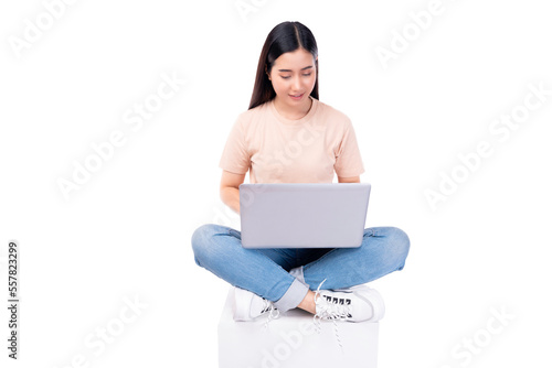 Happy young asian woman sitting on white chair with legs crossed and using laptop computer on light pink background copy space Full body young smiling happy female wearing t shirt and jeans lifestyle