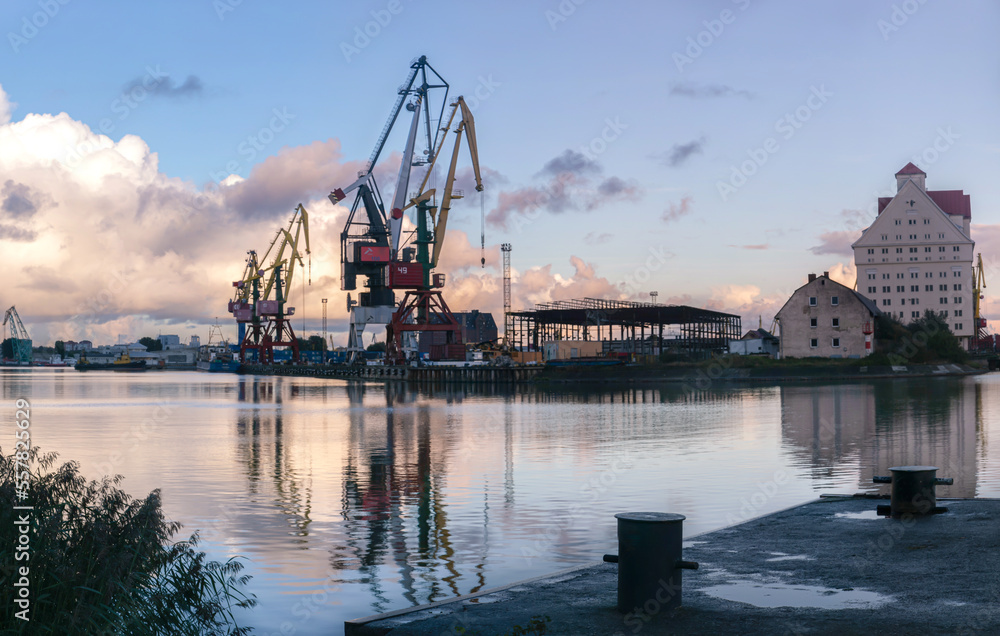 Cranes loaders of different colors load containers in the city port of Kaliningrad. A barge is moored at the port, which is waiting for cargo to go with goods for trade.