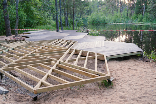 Walking area on screw piles, wooden frame, plastic terrace board on pond shore in park, construction site
