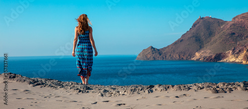 Woman with blue dress looking at panoramic coastline view of natural park, cabo de gata- Almeria,  Andalusia in Spain