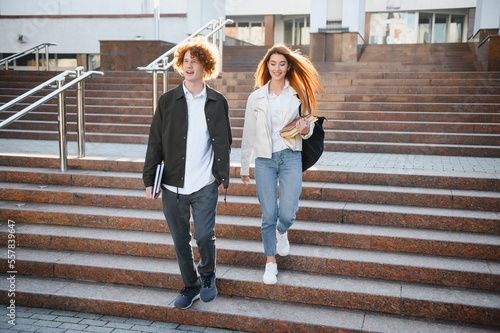 Front view of two students walking and talking in an university campus.