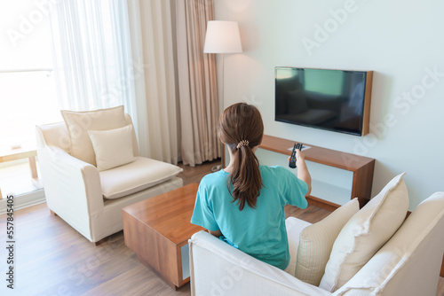 Woman relaxing on the couch, Girl using remote control and choosing TV show and movie series during rest on sofa in the morning. Apartment living concept