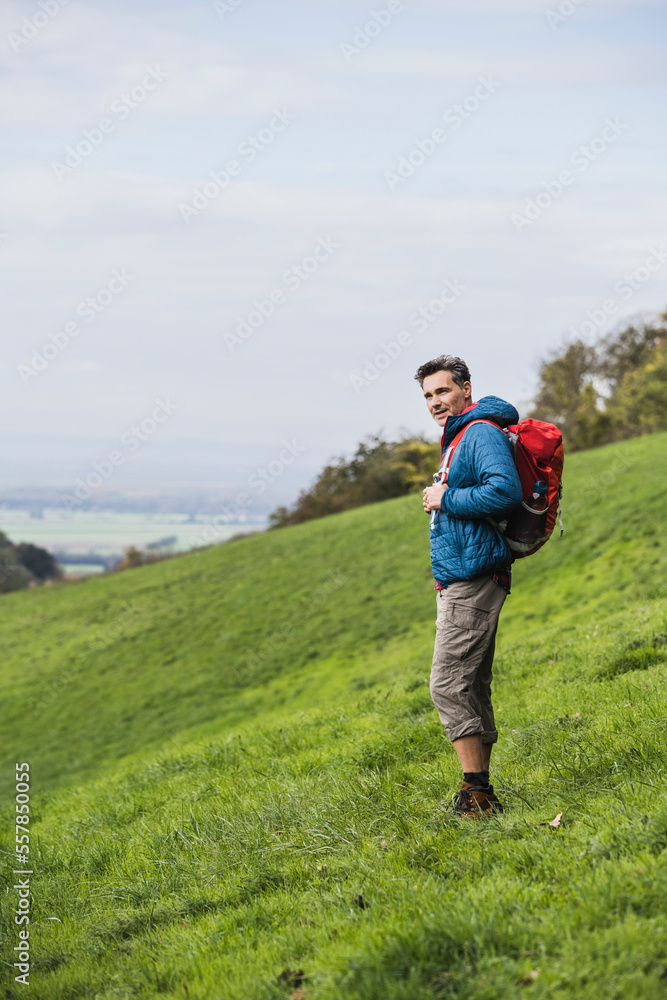 Mature man hiking with backpack on meadow by sky Mature man hiking with backpack on meadow by sky