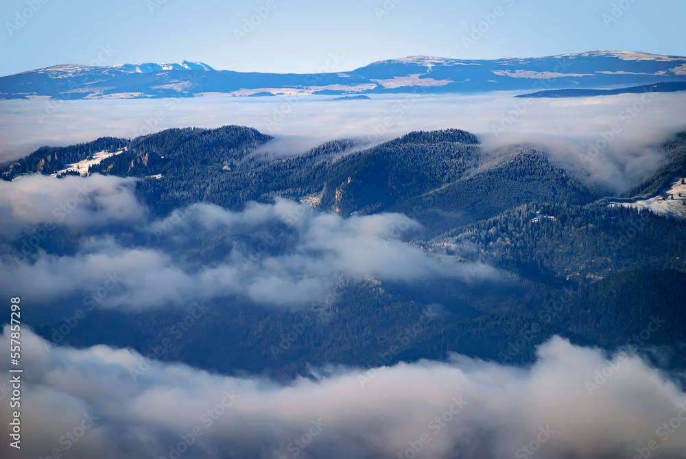 Fototapeta premium An epic ocean of clouds and fog in the winter mountains landscape, aerial view. Huge white clouds come in waves over the foggy valleys, mountain peaks rise over like islands. Dramatic overcast sky