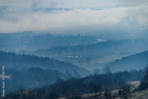 Hilly countryside with hilltops peeking through misty cover on autumn morning. First rays of light touching the trees and lifting morning mist above valleys. Serene moment in rural area in fall season © Creatikon Studio