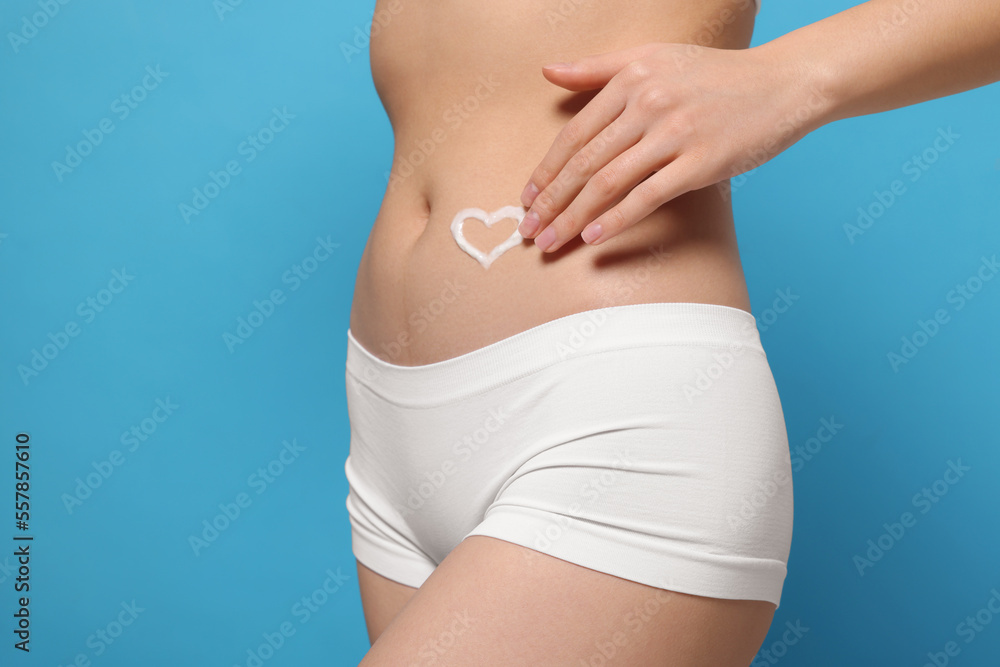 Woman with heart made of body cream on her belly against light blue background, closeup. Space for text