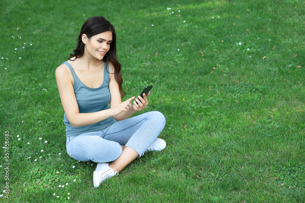 Young woman using smartphone on green grass outdoors Young woman using smartphone on green grass outdoors
