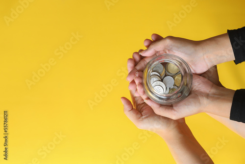 Quadro em tela Coins in two people hands on yellow background with copy space