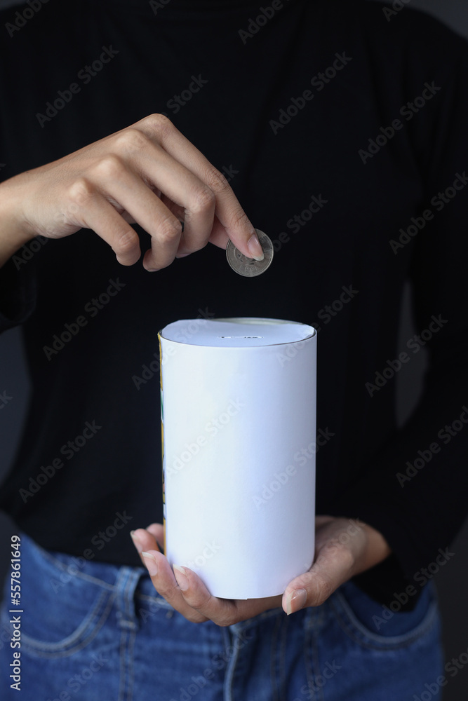 Close up of hand inserting coin in donation can for charity on dark gray background. Close up of hand inserting coin in donation can for charity on dark gray background.